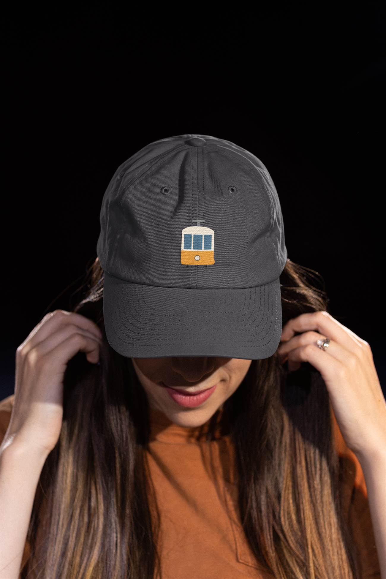 Black Lisbon Tram Cap with minimalist embroidery, worn by a woman adjusting the cap. A stylish unisex cap celebrating Lisbon's tram culture.