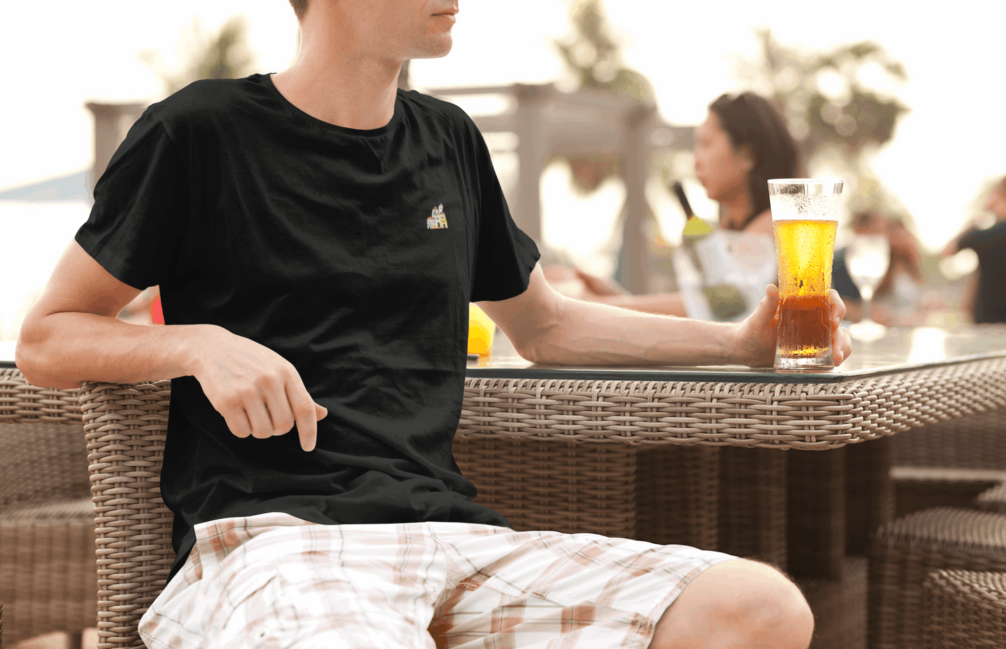 Man wearing a black Minimal Alfama Houses Unisex T-Shirt while relaxing with a drink, showcasing its casual fit and minimalist Lisbon design.