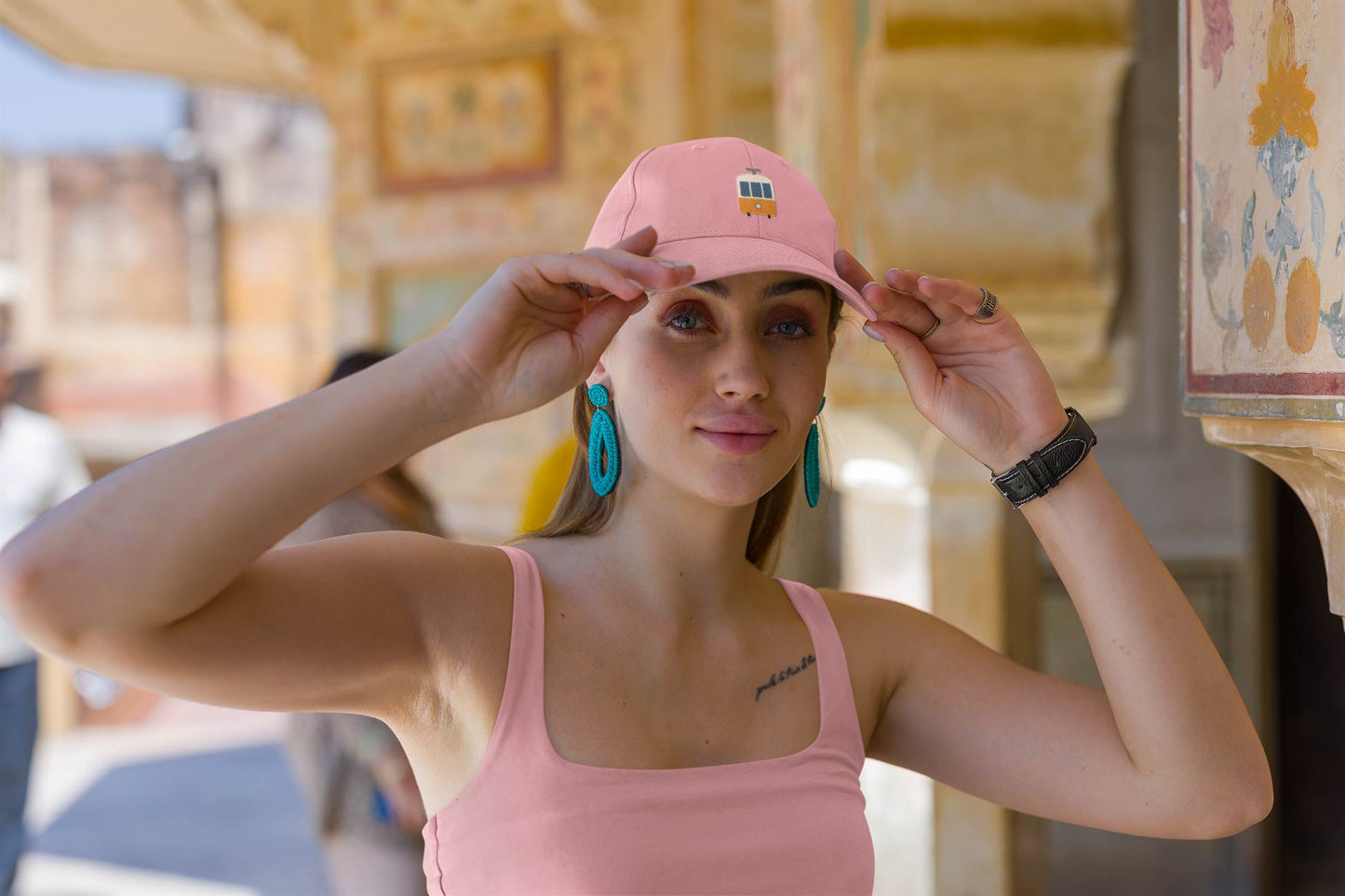 Pink Lisbon Tram Cap with minimalist embroidered tram logo, worn by a woman adjusting the cap. A stylish tribute to Lisbon's iconic tram.