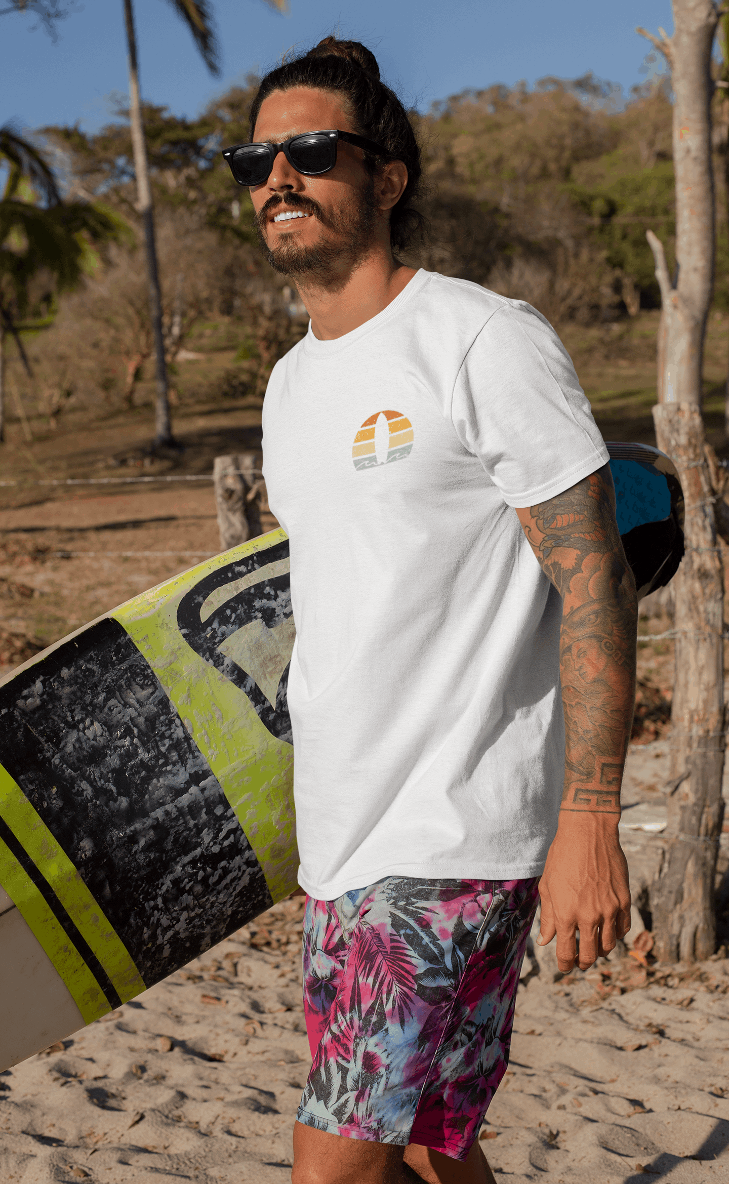 Man in a white Nazare Surf Minimal Organic T-shirt with a vintage surf logo, holding a surfboard on a tropical beach. Perfect for surf lovers and eco-conscious wearers.