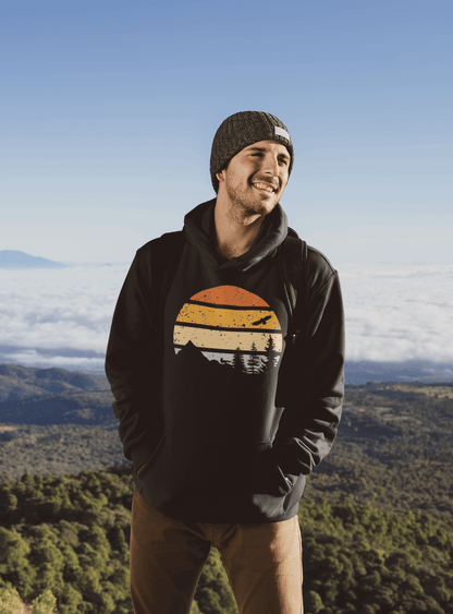 Black organic cotton hoodie featuring a vintage sunset and mountain design, worn by a man enjoying a scenic mountain view.