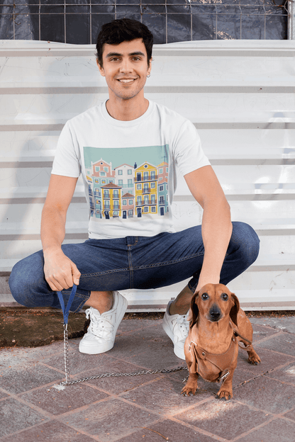 Smiling man in a white unisex T-shirt with Lisbon Alfama houses design, crouching with a dachshund. Organic cotton and eco-friendly style.