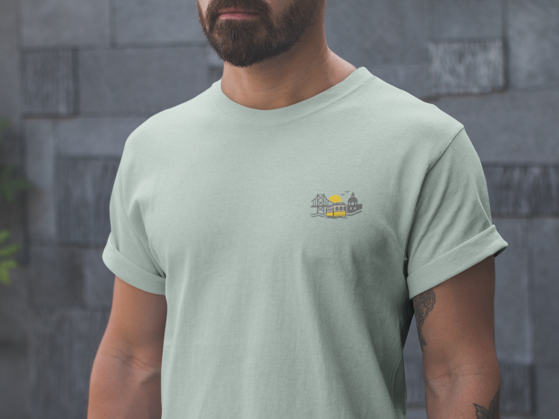 Man wearing a light green t-shirt with a small graphic on a stone wall background