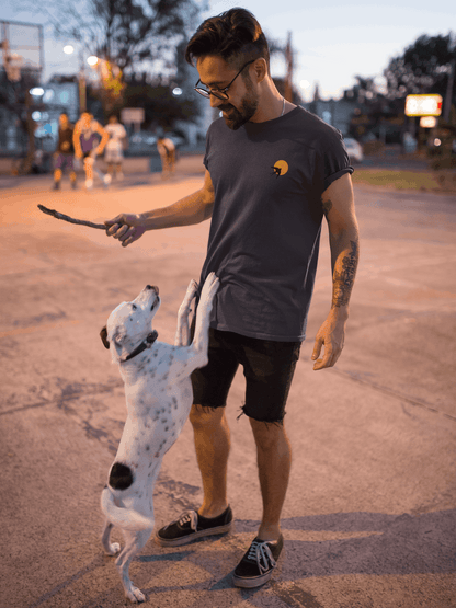 Man wearing a dark grey Andorinha T-Shirt playing with a dog outdoors. A unisex organic cotton tee with a minimalist swallow logo.