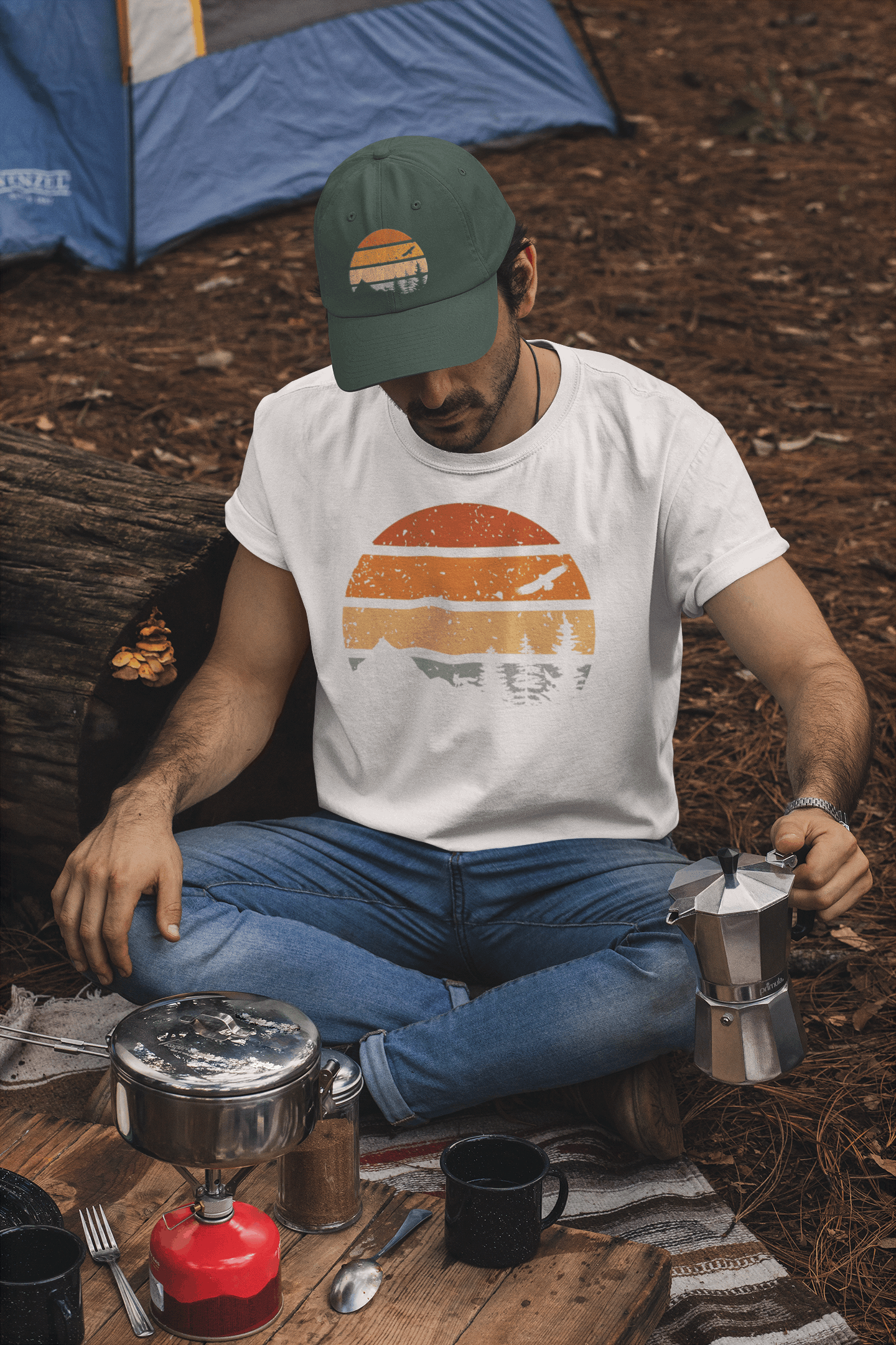Green Madeira Vintage Cap with a mountain logo, worn by a camper brewing coffee. A rugged and stylish cap for outdoor lovers.
