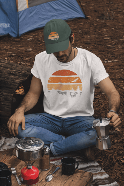 Green Madeira Vintage Cap with a mountain logo, worn by a camper brewing coffee. A rugged and stylish cap for outdoor lovers.