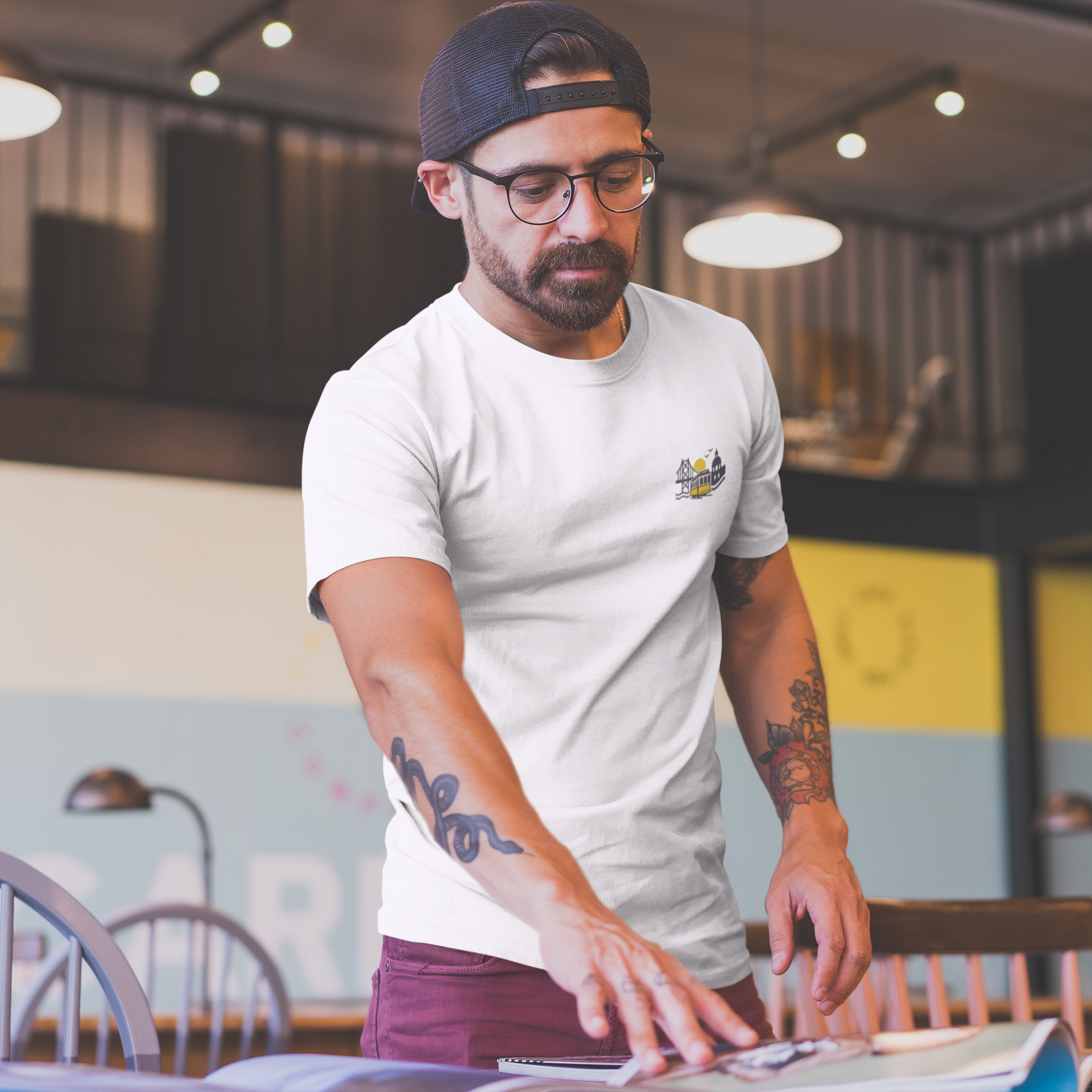 Man in a casual setting wearing a white t-shirt with a logo and a cap.