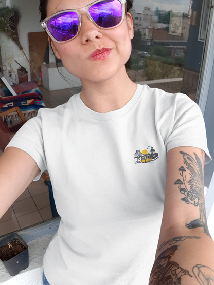 Person wearing a white t-shirt with a small logo, sitting indoors.